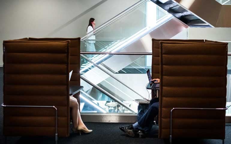 Two individuals seated in office chairs inside EHL. Somebody doing up the stairs in the background
