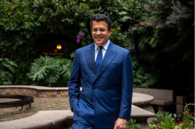 A well-dressed man stands confidently in a lush, botanical garden setting. Le contenu généré par l’IA peut être incorrect.